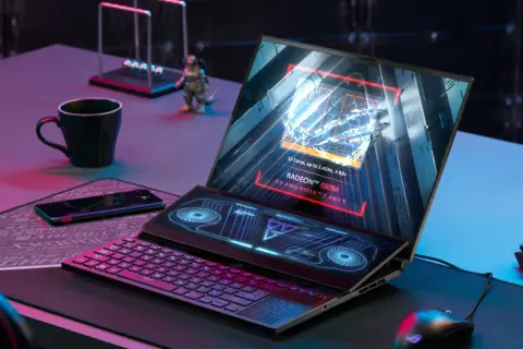Laptop z ekranem głównym wyświetlającym specyfikację AMD Radeon 680M na procesorze Ryzen 7/9. Obok klawiatura i dodatkowy ekran.