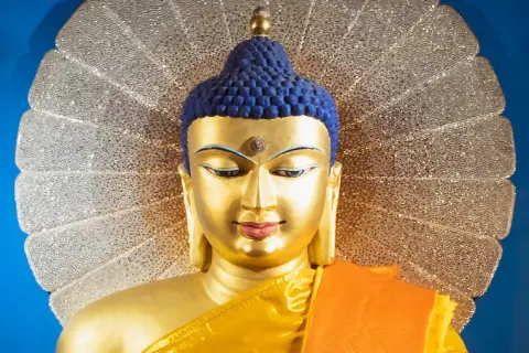 Goldene Buddha-Statue mit blauem Haar und orangefarbenem Gewand vor einem schimmernden Heiligenschein. Ein Wegweiser, wie werde ich buddhist.
