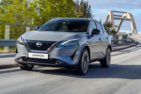 Szary Nissan Qashqai 2024 pędzi po moście z łukowatym wiaduktem w tle.