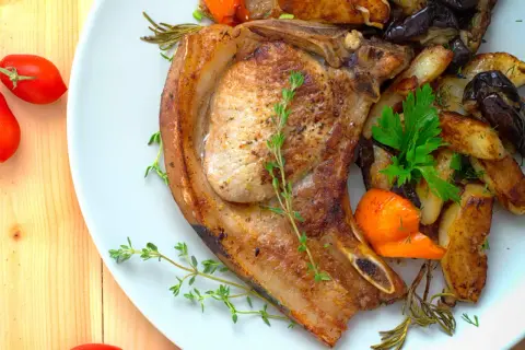 Une côte de porc juteuse, accompagnée de pommes de terre rôties, d'aubergines et de carottes, garnie d'herbes fraîches.