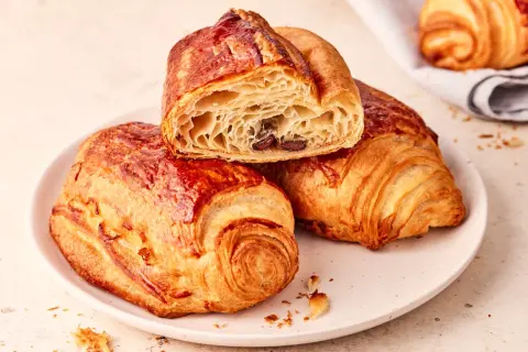 Złociste, chrupiące pain au chocolat na talerzu, jedno przekrojone, ukazujące puszyste wnętrze z kawałkami czekolady.