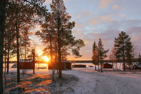 Solnedgång över camp alta kiruna. Röda stugor och snö täcker marken.
