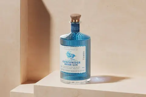 Elegancka butelka Drumshanbo Gunpowder Irish Gin, z niebieskim płynem i wytłoczonym jelonkiem, idealna na prezent dla miłośników ginów.