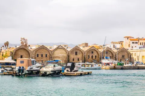 Port w Chanii, Kreta zimą. Łodzie zacumowane przy kamiennych budynkach, w tle góry.