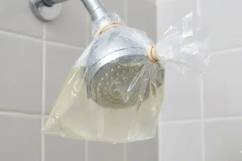 Doccia con soffione avvolto in un sacchetto pieno di liquido, per rimuovere residui di autoabbronzante che si toglie con l'acqua.