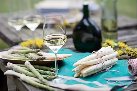 Ein Glas Weißwein steht neben frischem Spargel auf einem Holztisch. Perfekt für den Genuss von Wein zum Spargel.
