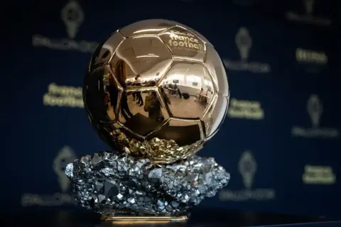 Złota Piłka, symbol triumfu na gali, lśni na tle logo France Football.