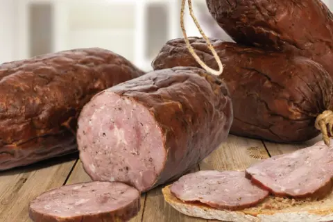 Kiełbasa żywiecka, wędzona, z widocznym przekrojem i plastrami na chlebie, prezentuje się apetycznie na drewnianym stole.