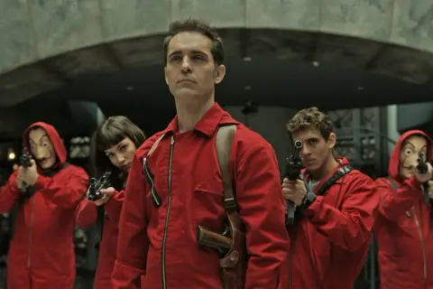 Das Team vom Haus des Geldes Berlin ist bereit. Fünf Personen in roten Overalls und Masken halten Waffen.