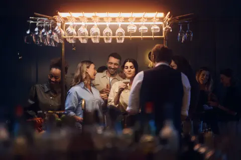 Glada gäster minglar och skrattar vid baren på Gothia Towers Skybar. Glas hänger i taket, redo för drinkar.
