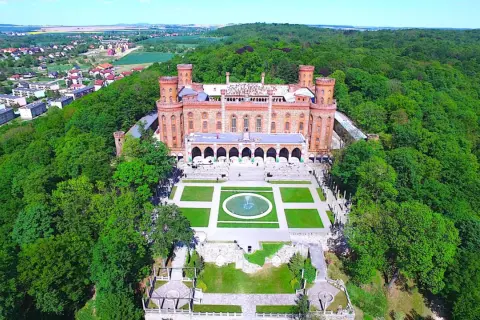 Kamieniec Ząbkowicki zamek, otoczony bujną zielenią, prezentuje swoją neogotycką architekturę z wieżami i arkadowym dziedzińcem.
