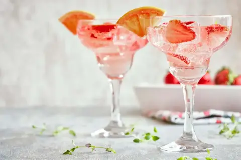 Orzeźwiające drinki z truskawkami i plasterkami grejpfruta, idealne na letnie popołudnie. W tle widać świeże truskawki.
