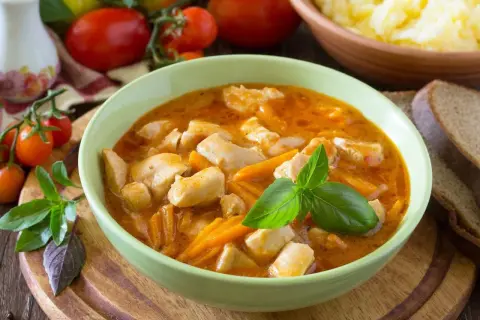Aksamitny gulasz z piersią z kurczaka z marchewką, udekorowany bazylią. Obok kromki chleba i miska purée ziemniaczanego.