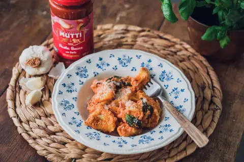 En tallrik med krämig tortellini, toppad med parmesan och färska örter. Bredvid står en burk Mutti tomatsås och vitlök, perfekt för ett enkelt tortellini recept.
