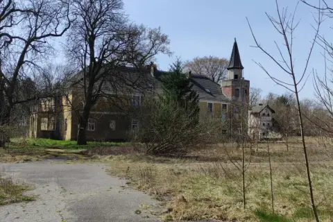 Opuszczony pałac w Torzymiu, z charakterystyczną wieżą, otoczony dziką roślinnością.