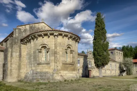 Antigua iglesia románica en Ferreira de Pantón, Lugo. Fachada de piedra con arcos y un ciprés alto.