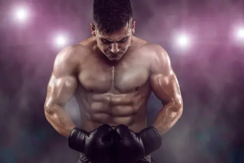 A muscular boxer with a defined boxer physique, wearing black gloves, looks down intensely under stadium lights.