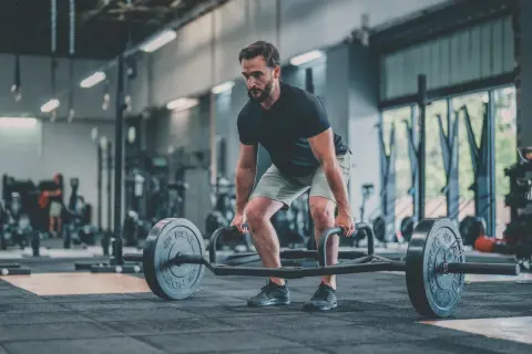 Un homme concentré effectue un dead lift avec une barre hexagonale dans une salle de sport.