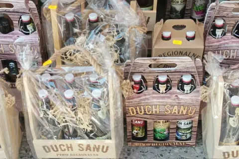 Drewniane skrzynki i opakowania z butelkami regionalnego piwa "Duch Sanu", ozdobione sznurkiem i folią.
