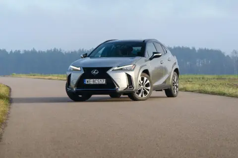 Srebrny Lexus UX 250h na krętej drodze, z lasem w tle.