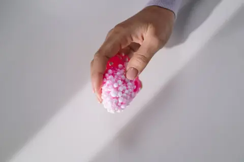 Dłoń trzyma różowy slime z kulkami, który wygląda jak mała, puszysta chmurka.