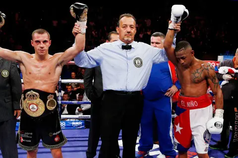 Referee raises the winner's hand after a boxing match. The boxer on the left, wearing a championship belt, achieved a win by decision.