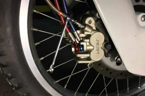 Zbliżenie na zacisk hamulcowy motocykla z przewodami hamulcowymi i kluczem.