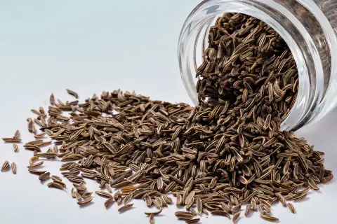 Semi di cumino nero versati da un barattolo di vetro. Scopri come mangiarli per un sapore unico.