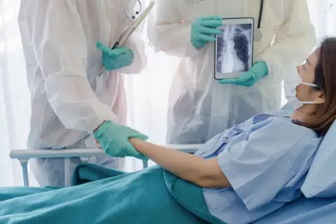 Lekarze w kombinezonach ochronnych wspierają pacjentkę w szpitalu, pokazując jej zdjęcie płuc na tablecie. Nadzieja na powrót do zdrowia dzięki leczeniu, być może z użyciem remdesivir.