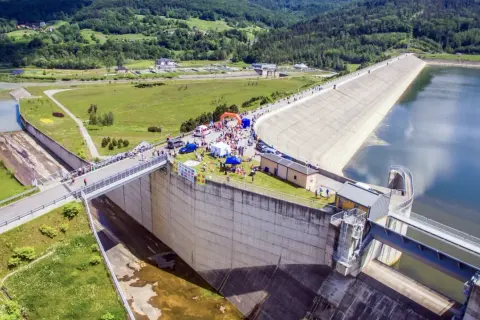 Wydarzenie sportowe przy zaporze w Świnnej Porębie. Tłum ludzi, namioty i pomarańczowa brama startowa na tle monumentalnej budowli.