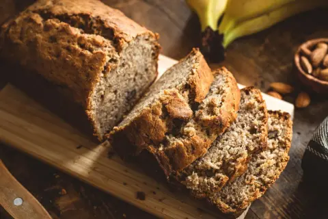Saftiges Bananenbrot, perfekt für ein Bananenbrot Rezept ohne Zucker. Daneben liegen Mandeln und reife Bananen.