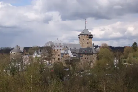 Das Schloss Burg an der Wupper, eine imposante Burganlage mit Bergfried und vielen Gebäuden, thront über Bäumen.