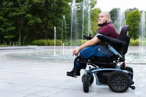 Mężczyzna na wózku inwalidzkim patrzy w dal, siedząc przy fontannie.
