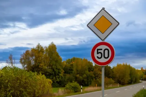 Panneau de priorité à droite et limite de vitesse à 50 km/h sur une route bordée d'arbres aux couleurs d'automne.