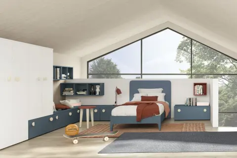 Un accogliente **letto sotto la finestra** in una stanza moderna con armadio bianco, librerie blu e dettagli sportivi come pallone e skateboard.