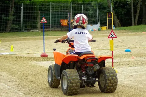 Dziecko w kasku na quadzie uczy się zasad ruchu drogowego na torze. To jego pierwsza karta motorowerowa.