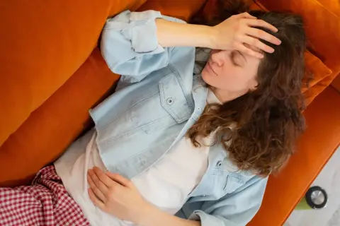 Kobieta z ręką na czole leży na pomarańczowej kanapie, wyczerpana przewlekłym stresem. Szuka ulgi i leczenia.