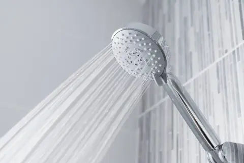 A chrome shower head sprays water, questioning if shower heads are universal.