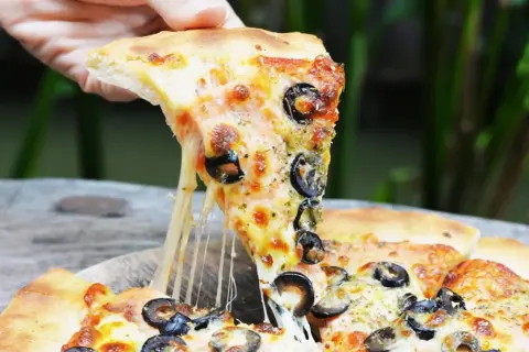 Ciągnący się ser z kawałka pizzy capriciosa z oliwkami, podnoszony ręką.