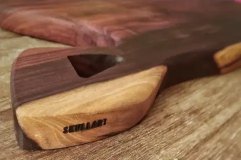 Tabla de cortar artesanal con veta de madera africana, marcada con "SKULLART".