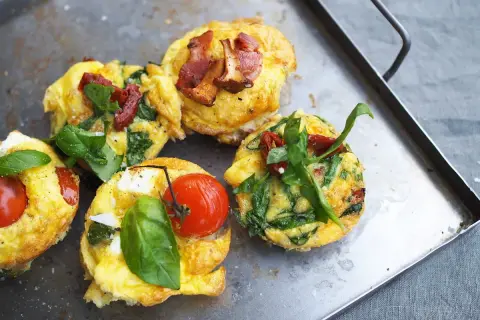 Matiga muffins med ägg, spenat, tomat och bacon på en plåt. Perfekt för en mättande frukost eller brunch.