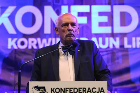 Mężczyzna w garniturze i muszce przemawia na tle napisu "KONFEDERACJA".