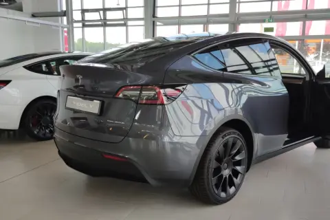 Szary Tesla Model Y z otwartymi drzwiami, obok biały Model 3. Wymiary tego SUV-a są idealne do miasta i na dalsze trasy.