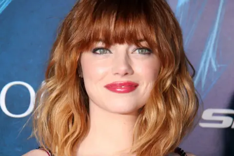 Emma Stone luce un vibrante pelo naranja en cascada, un estilo que realza su belleza natural.