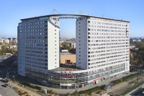 Dom wschodzącego słońca, nowoczesny budynek z charakterystycznym mostem łączącym dwie wieże, z widokiem na miasto.