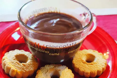 Bicchiere di cioccolata calda con acqua senza fecola, accompagnata da biscotti su un piatto rosso.