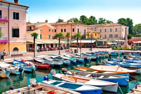 Barche ormeggiate nel **bardolino hafen**, con edifici colorati e palme sullo sfondo.