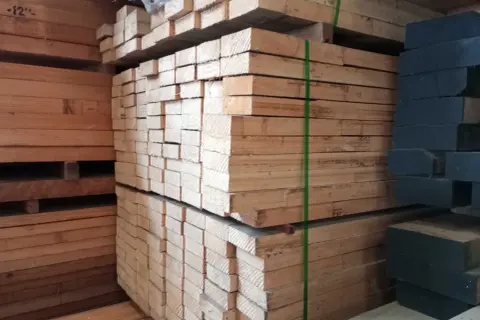 Piles of light-colored lumber, possibly madera ayous, are stacked high. A stack of dark wood is visible on the right.