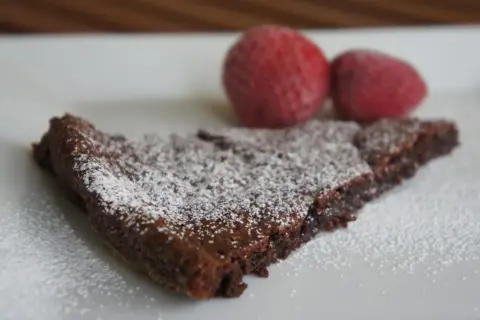 En bit kladdkaka, pudrad med florsocker, med två jordgubbar i bakgrunden. Perfekt för dig som älskar kladdkakecookies utan choklad.