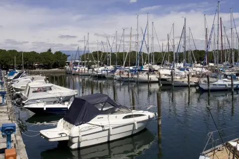 Barche a vela e a motore ormeggiate nella marina di Porto San Giorgio, con alberi che si stagliano contro il cielo azzurro.